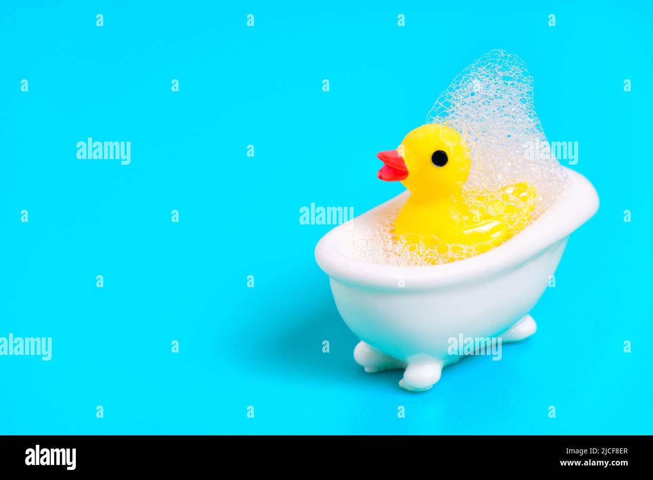 Yellow baby duck in a tiny white bathtub covered with soap bubbles. Children`s bath time concept